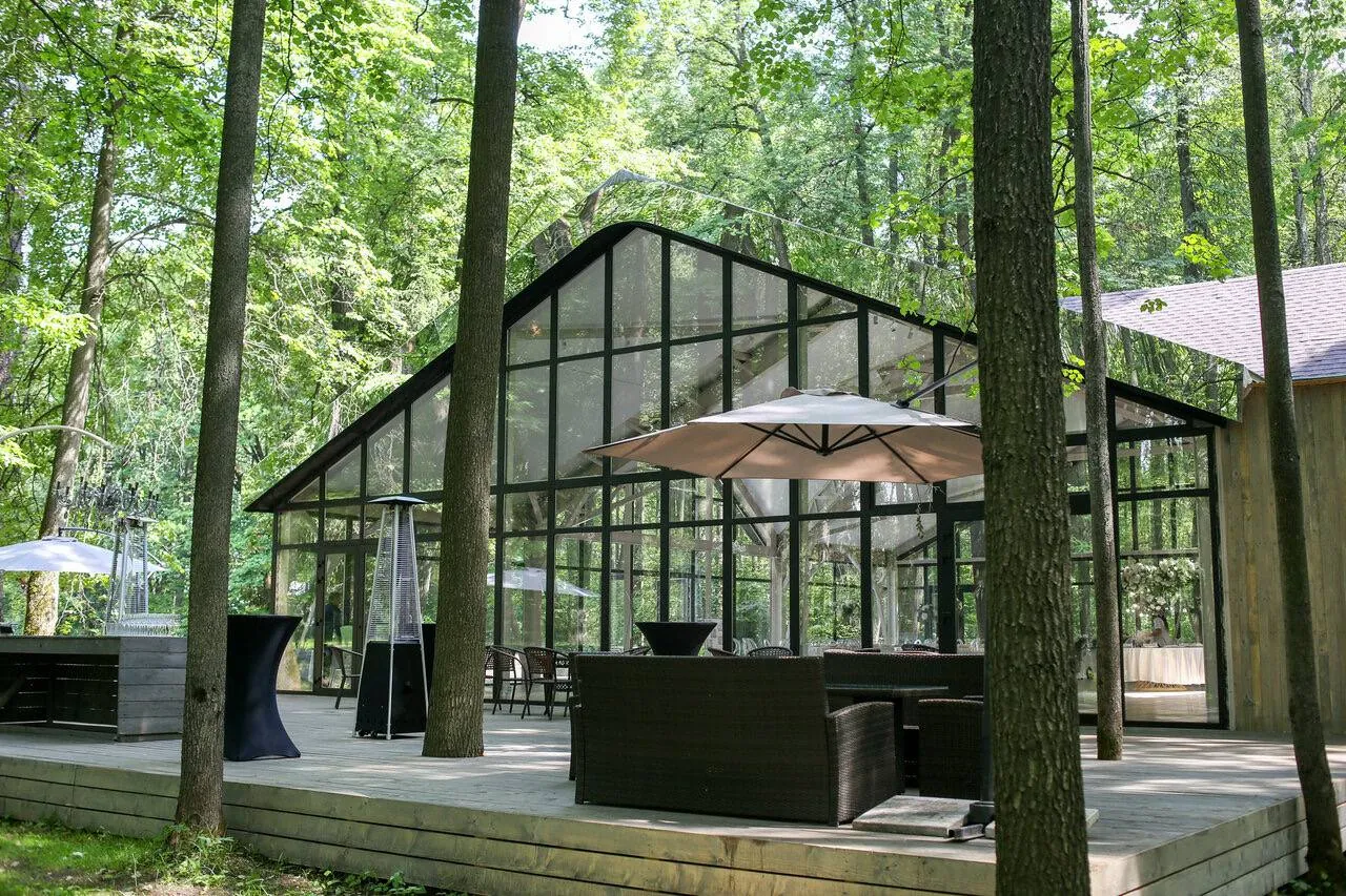 Оранжерея Les Event House среди деревьев: стеклянный павильон и терраса с зонтом